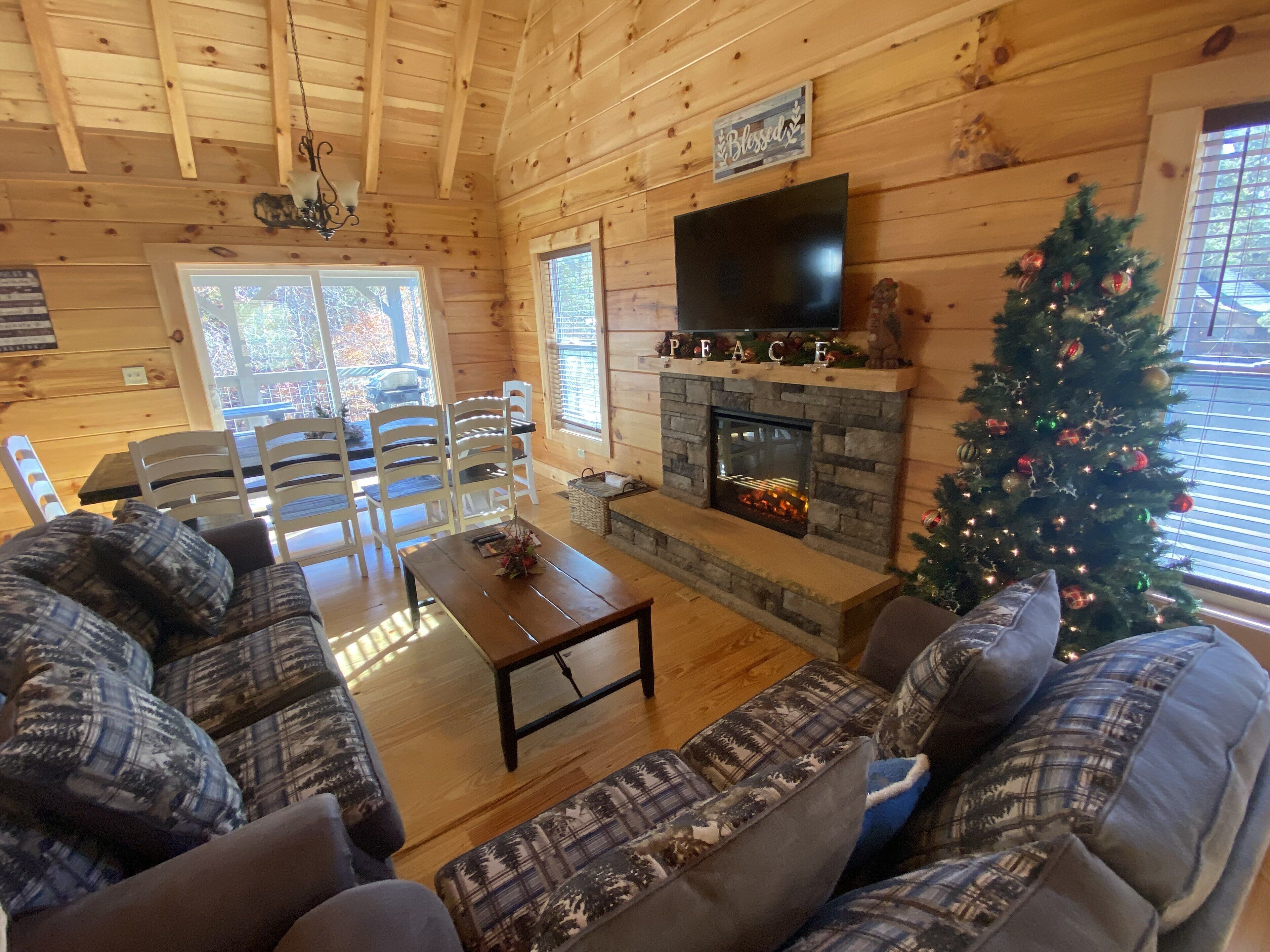 Accogliente interno di una baita in legno con camino, albero di Natale e zona pranzo.