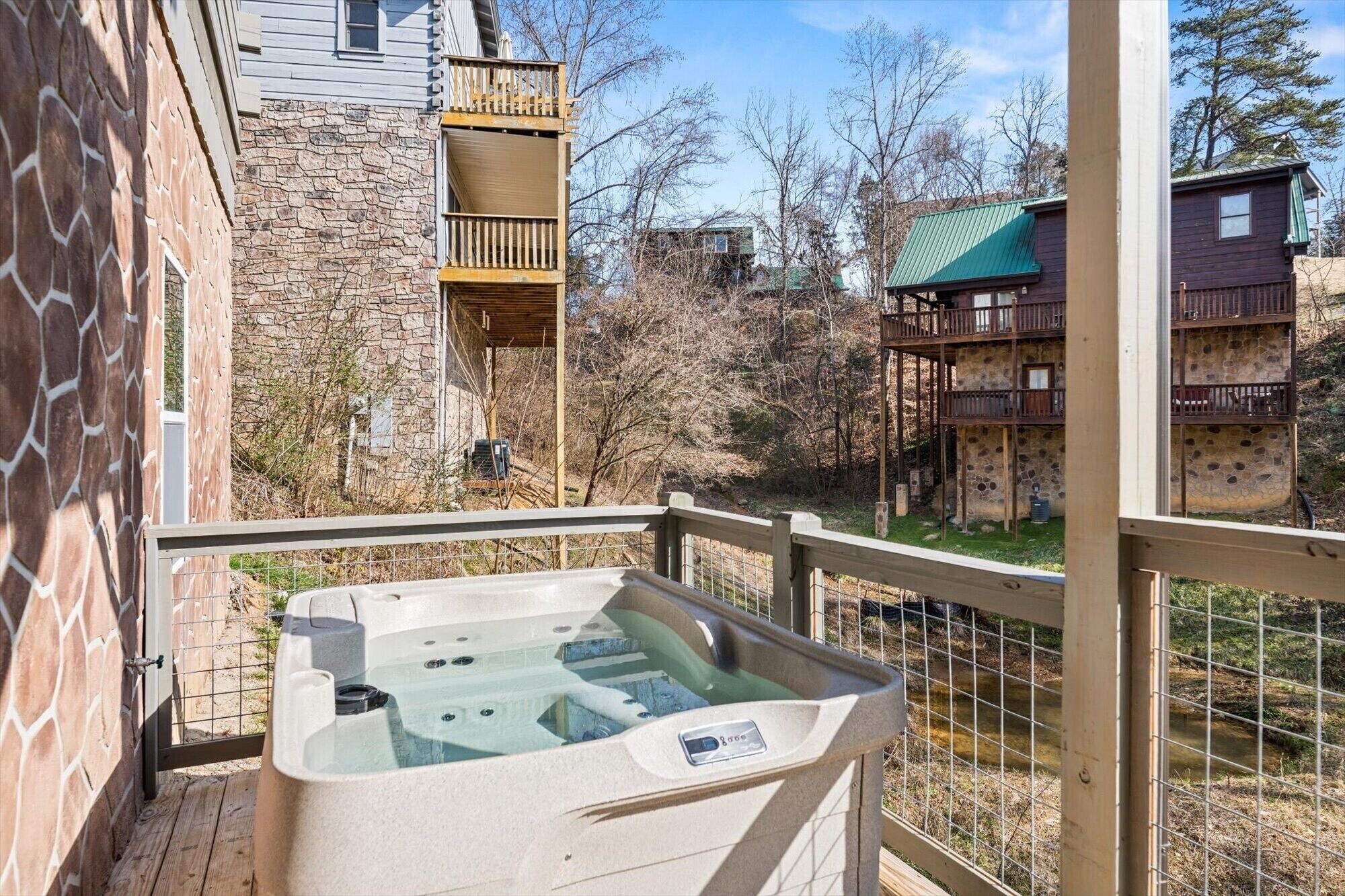 Un jacuzzi en un balcón con pared de piedra y barandilla de madera.