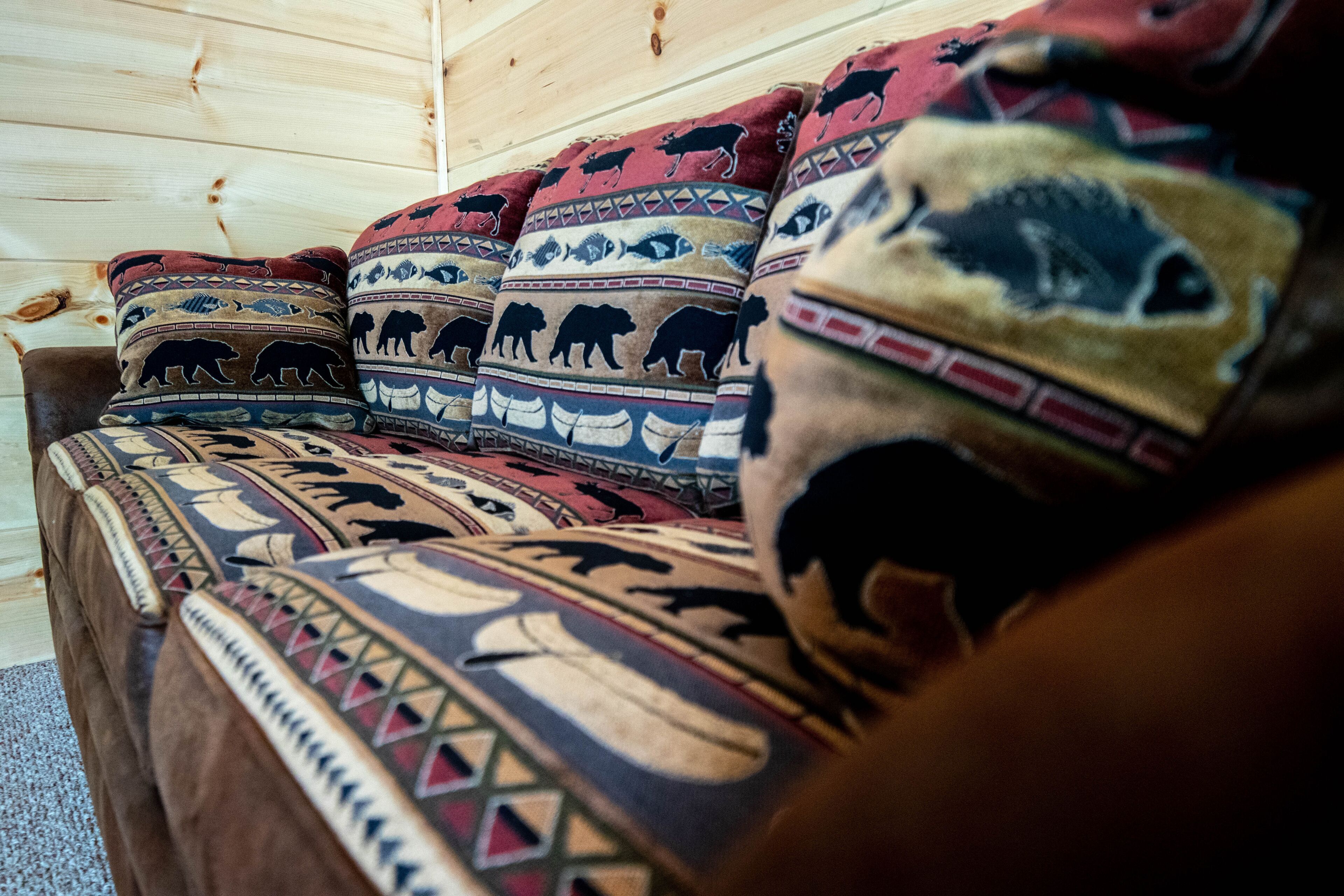 Interior de una cabaña de madera con un sofá decorado con cojines estampados de motivos animales.