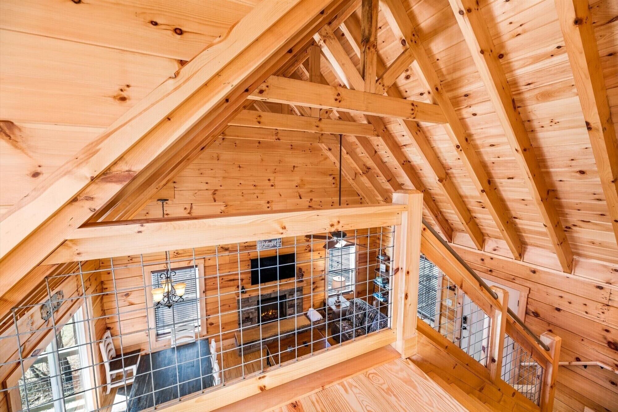Interior de madera con techo inclinado, baranda metálica y una ventana.