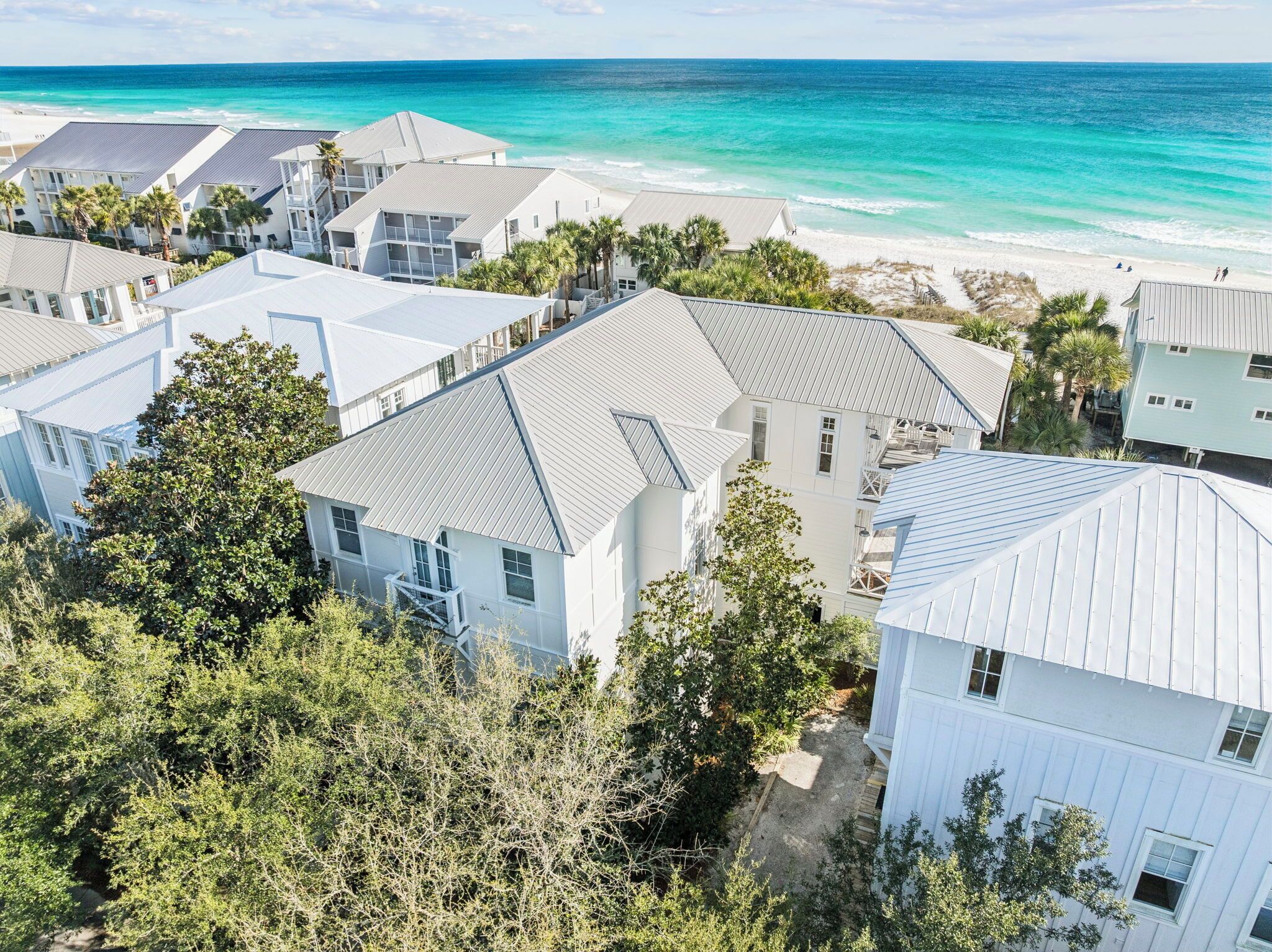 Un quartier résidentiel situé sur la côte, avec de nombreux bâtiments blancs, dont certains ont des toits inclinés, et une plage en arrière-plan.