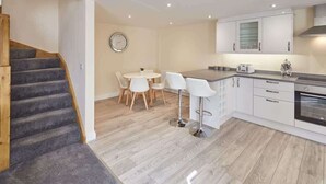 Une cuisine moderne avec des meubles blancs, un escalier en bois et un coin repas avec des chaises blanches.
