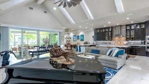 Een ruime woonkamer met een pooltafel, een moderne keuken met donkere kastjes en een plafondventilator.