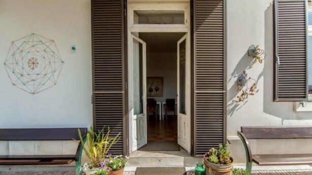 A building entrance with open shutters, a geometric wall decoration, and potted plants on the ground. - Coimbra Guesthouse (Coimbra)