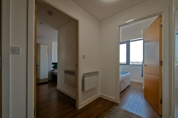 A hallway leading to a bedroom with a window, a radiator, and a door.