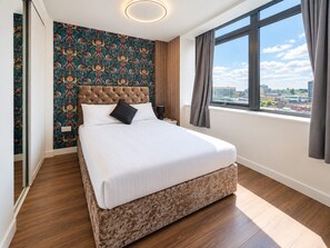 A hotel room with a large bed, a city view, a patterned wallpaper, and a modern ceiling light. - 2 Bedroom Central Apartment  (Liverpool)