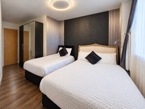 Habitación de hotel con dos camas, un espejo, piso de madera y una lámpara de techo moderna.