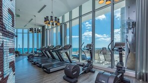 A gym with treadmills, elliptical machines, and weight equipment, large windows with a view of the sky and a building. - Hyde Side Ocean View 1 Bedroom Condo by RedAwning (Hollywood)