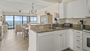 A spacious kitchen with white cabinets, a granite countertop, and a view to the outside. - Oceana 1-Upgraded 2 Bedroom Ocean Front Oceana Condo with Outdoor Pool! (Ocean City)