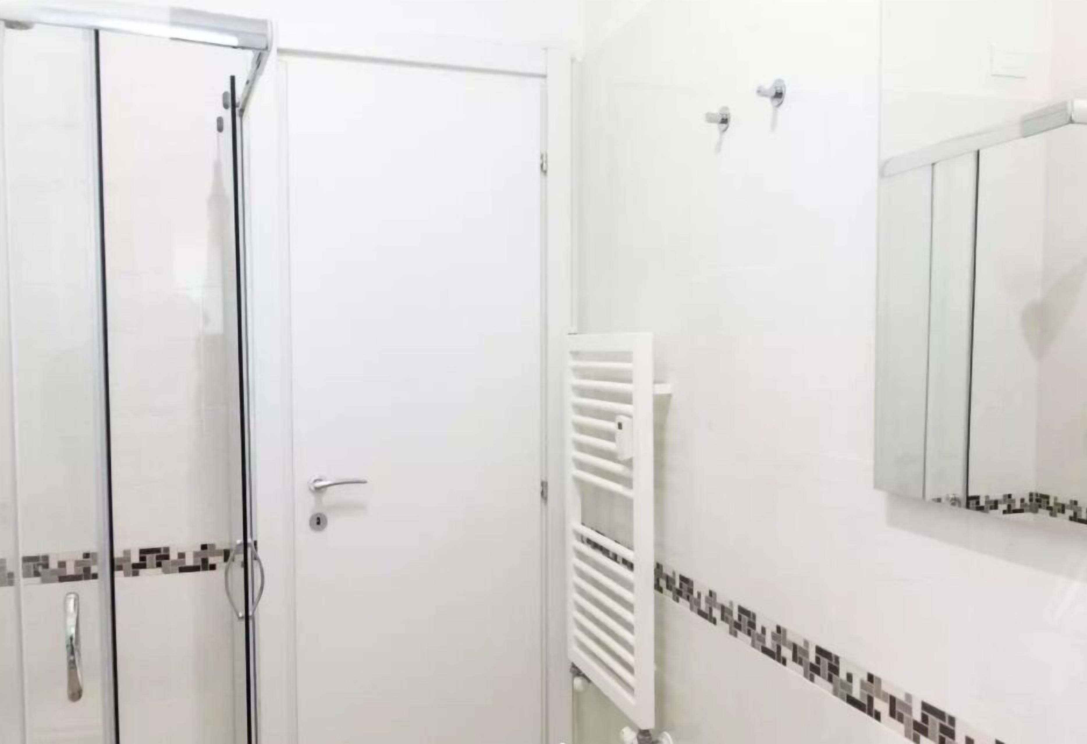 A bathroom with a glass shower enclosure, a white towel rack, and a tiled backsplash.