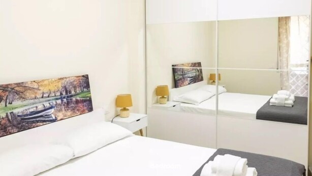 A hotel room with a bed, a bedside table with a lamp, a mirror, and a painting on the wall. - Via delle Medaglie d'Oro (Rome)