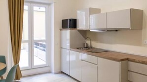 A compact kitchen with white cabinets, a wooden countertop, and a window with curtains. - Via delle Medaglie d'Oro (Rome)