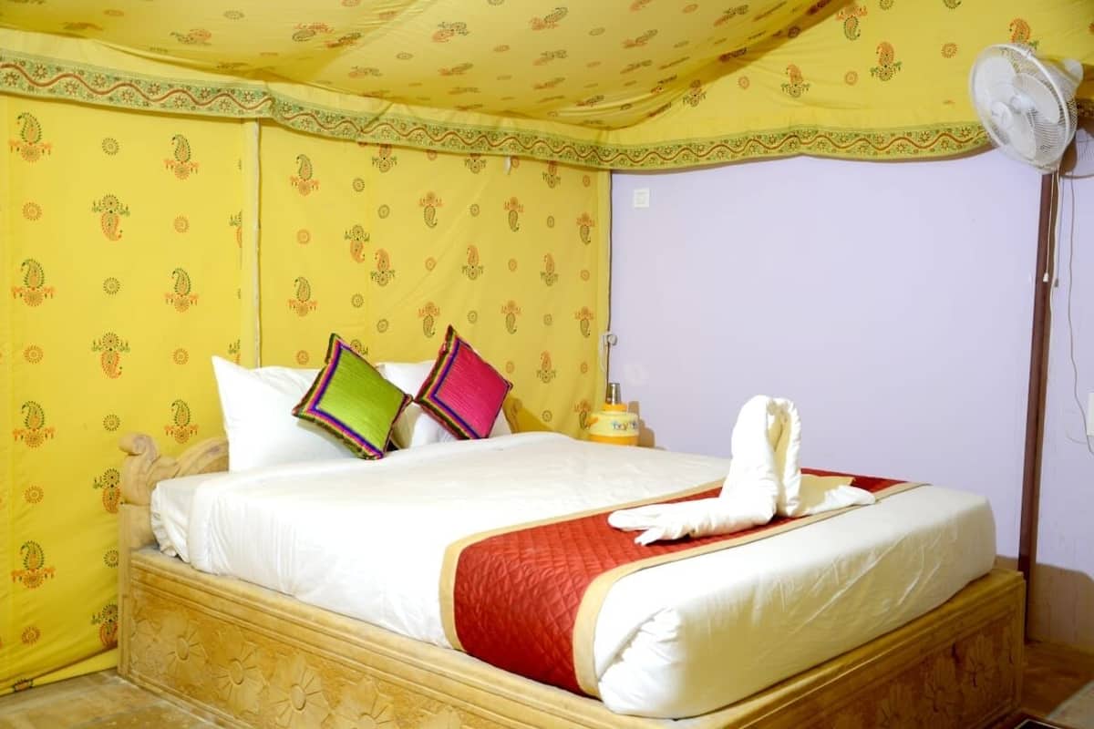 A hotel room with a bed, pillows, a fan, and a towel.