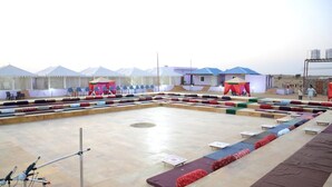 A large outdoor seating area with multiple rows of chairs and tables, tents in the background, and a clear sky. - Ozaki Desert Camp Jaisalmer  (Jaisalmer)