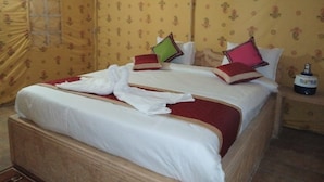 A bed with white and red bedding, a wooden headboard, and a nightstand with a bottle. - Ozaki Desert Camp Jaisalmer  (Jaisalmer)