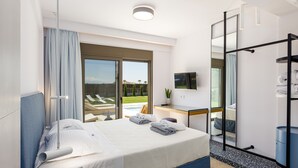 Une chambre d’hôtel moderne dotée d’un grand lit, d’un bureau avec un téléviseur à écran plat, d’un dressing et offrant une vue sur une piscine et un espace verdoyant.