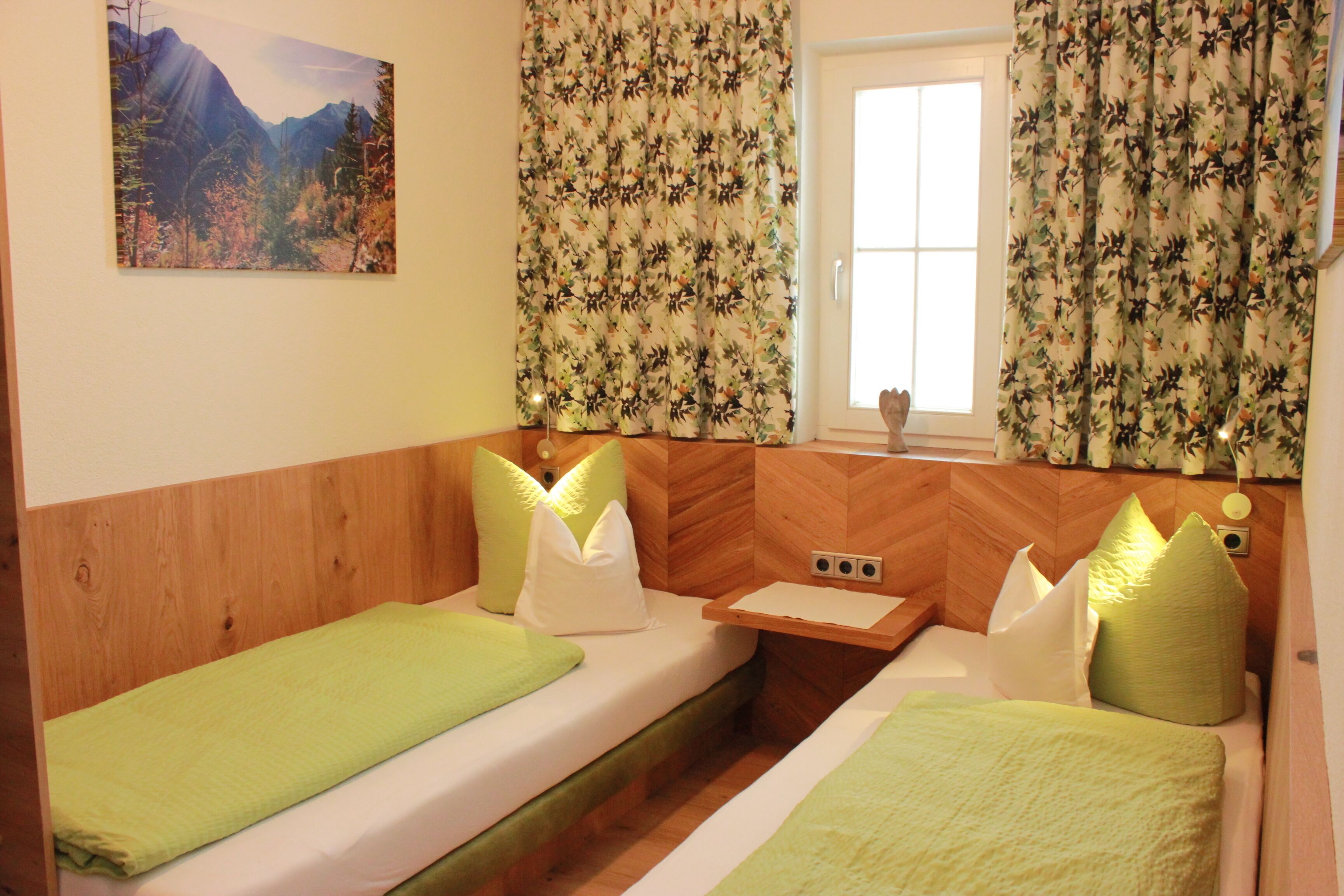 A room with two beds, a wooden headboard, a small table, and a window with curtains.