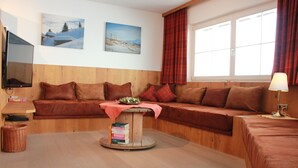 A cozy room with a wooden sofa, a small table with a book, and a window with curtains. - Winter dream vacation apartment in the Zillertal in direct proximity to the Horbergbahn ski lift (Schwendau)
