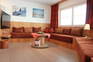 A cozy room with a wooden sofa, a small table with a book, and a window with curtains. - Winter dream vacation apartment in the Zillertal in direct proximity to the Horbergbahn ski lift (Schwendau)