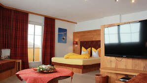 A modern hotel room with a large bed, a flat-screen TV, a wooden headboard, and a window with curtains. - Winter dream vacation apartment in the Zillertal in direct proximity to the Horbergbahn ski lift (Schwendau)