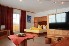 A modern hotel room with a large bed, a flat-screen TV, a wooden headboard, and a window with curtains. - Winter dream vacation apartment in the Zillertal in direct proximity to the Horbergbahn ski lift (Schwendau)