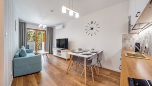 A modern living room with a sofa, TV, dining table, and kitchen area with a clock and patterned backsplash. - Apartamenty Sun & Snow Nautikka Park (Krynica Morska)