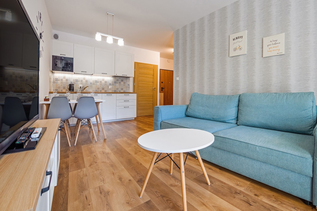A modern living room with a blue sofa, a white coffee table, and a dining area with a wooden table and chairs.
