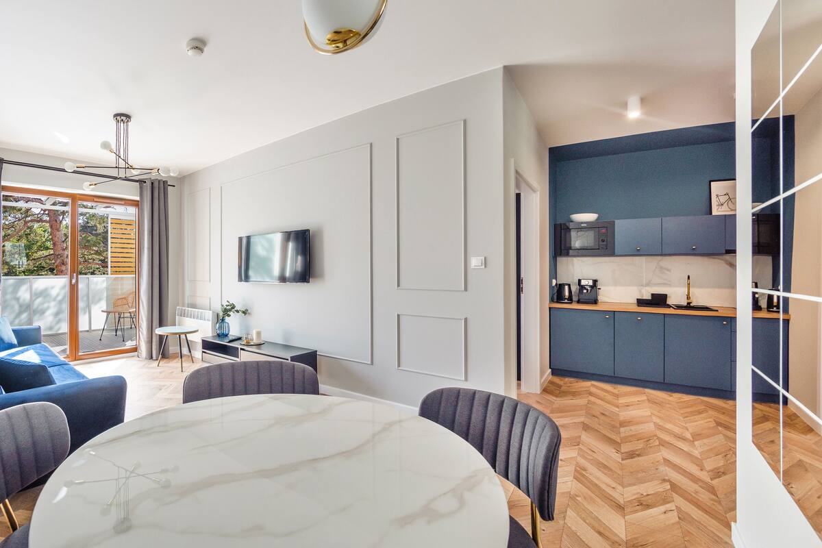 A modern apartment with a dining area, a kitchen, and a living room with a sofa and a TV.