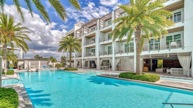A swimming pool surrounded by palm trees and a multi-story building with balconies.