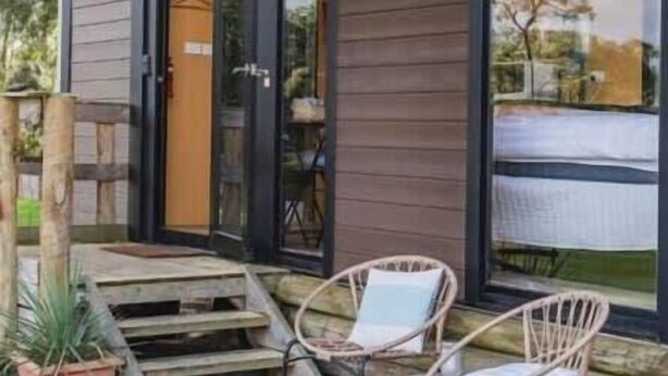 Un edificio moderno con amplios ventanales, una terraza de madera y dos sillas de mimbre.
