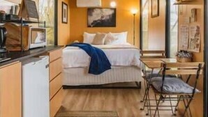 Una habitación de hotel compacta con cama, un escritorio pequeño, una silla y una kitchenette.