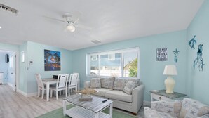 A living room with a light blue wall, a ceiling fan, a dining table with chairs, a sofa, a coffee table, and a lamp. - MT Under the Sea 1 bedroom 1 bath in multi-family near beach (Fort Myers Beach)