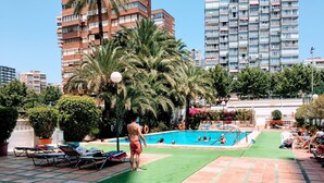 A swimming pool area with lounge chairs, palm trees, and a view of tall residential buildings. - GEMELOS 1 MODERN SEAVIEWS R084 (Benidorm)