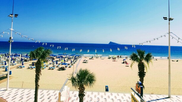 A beach with rows of blue umbrellas and lounge chairs, a clear blue sky, and a calm sea. - GEMELOS 1 MODERN SEAVIEWS R084 (Benidorm)