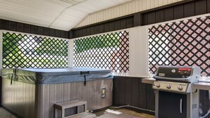 A covered outdoor area with a hot tub, a grill, and a small wooden table. - Home of Champions: HOF Village Comfort (Canton)