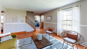A spacious living area with a wooden floor, a sofa, a chair, and a coffee table. There is a staircase leading to an upper level. - Home of Champions: HOF Village Comfort (Canton)