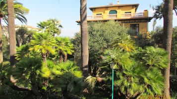 A yellow building with a balcony, surrounded by palm trees and other greenery.
