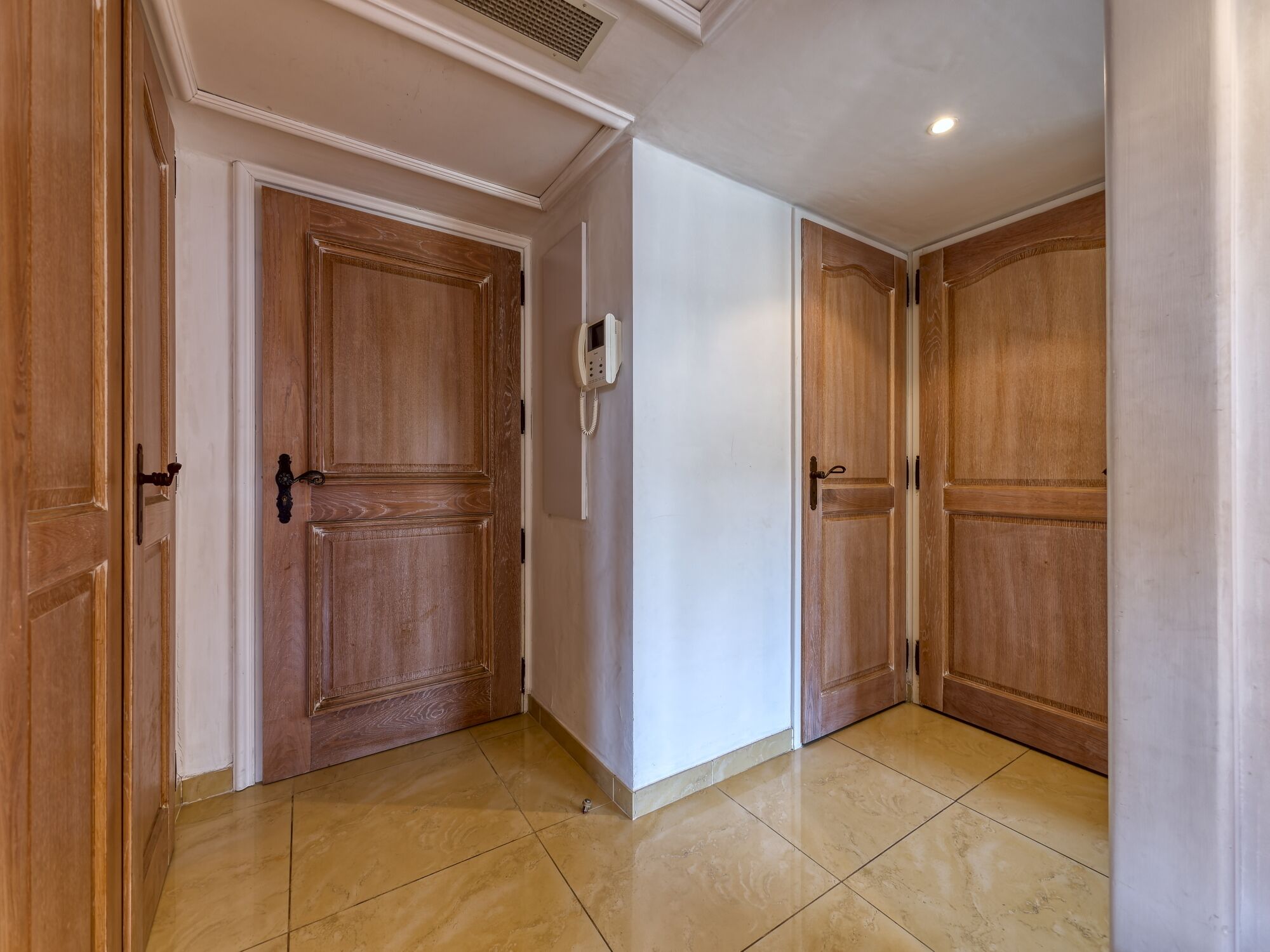A hallway with wooden doors, a white wall, and a tiled floor.