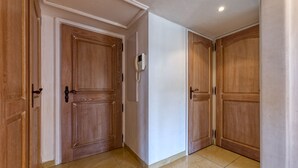 Un pasillo con puertas de madera, una pared blanca y un piso de baldosas.