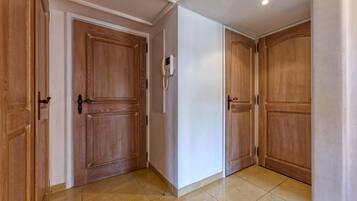 A hallway with wooden doors, a white wall, and a tiled floor.