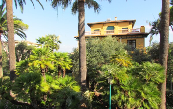 A yellow building with a balcony, surrounded by palm trees and other greenery.