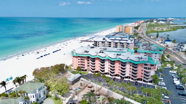 Un hotel frente a la playa con varios balcones, un estacionamiento y una playa al fondo.