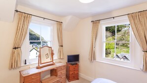 A bedroom with a bed, a wooden dresser, a television on a stand, and a window with curtains. - Lorna Doone Cottage, Lynmouth (Lynmouth)