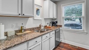 A kitchen with white cabinets, a granite countertop, a coffee maker, and a window with blinds. - Modern 2 BR Condo - 2 block from San Marco (Jacksonville)