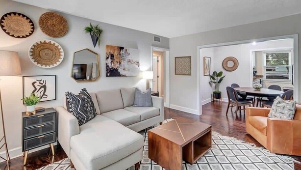 A modern living room with a sectional sofa, a coffee table, and a dining area with a table and chairs. - Modern 2 BR Condo - 2 block from San Marco (Jacksonville)
