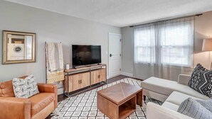 A living room with a sofa, a coffee table, a TV, and a cabinet. - Modern 2 BR Condo - 2 block from San Marco (Jacksonville)
