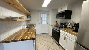 A modern kitchen with wooden countertops, white cabinets, a microwave, a stove, and a coffee maker.