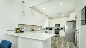 A modern kitchen with white cabinetry, a central island, stainless steel appliances, and a wooden floor. - Stunning Ver La Mer - Direct Ocean & Beach Access! (Surfside Beach)