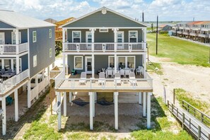 Une maison à deux étages située en bord de mer, dotée d’un balcon et d’un espace extérieur aménagé pour s’asseoir.