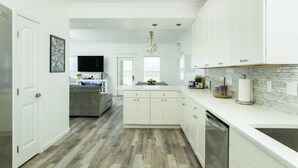 A modern kitchen with white cabinetry, a central island, and a backsplash. - Stunning Ver La Mer - Direct Ocean & Beach Access! (Surfside Beach)